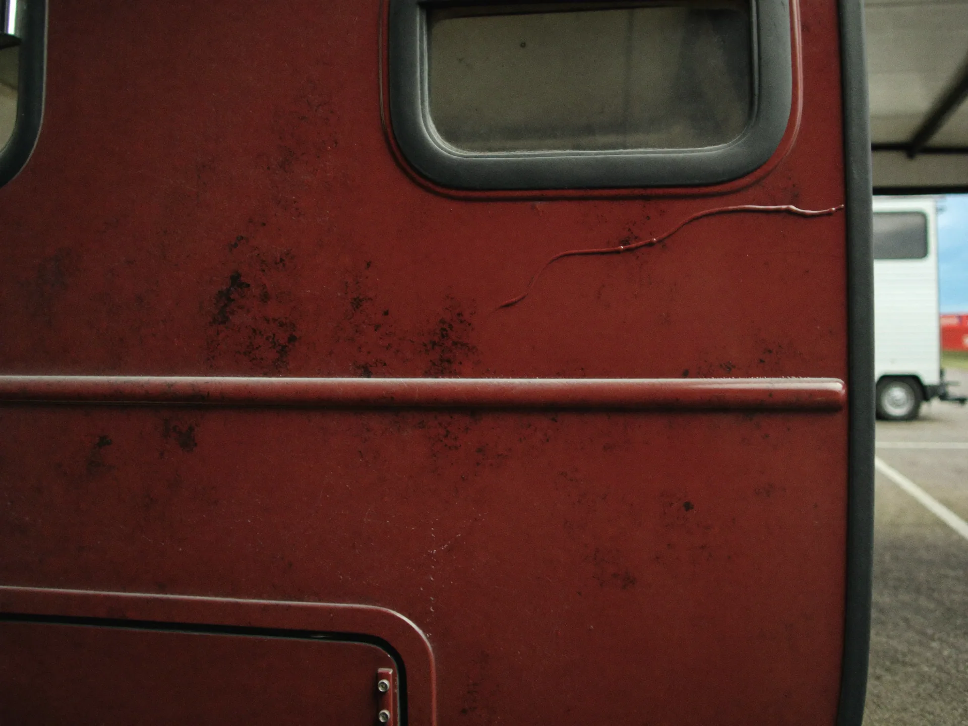 Close view along an awning housing and the wall panel beneath it on a dark red Class A mot during RV detailing