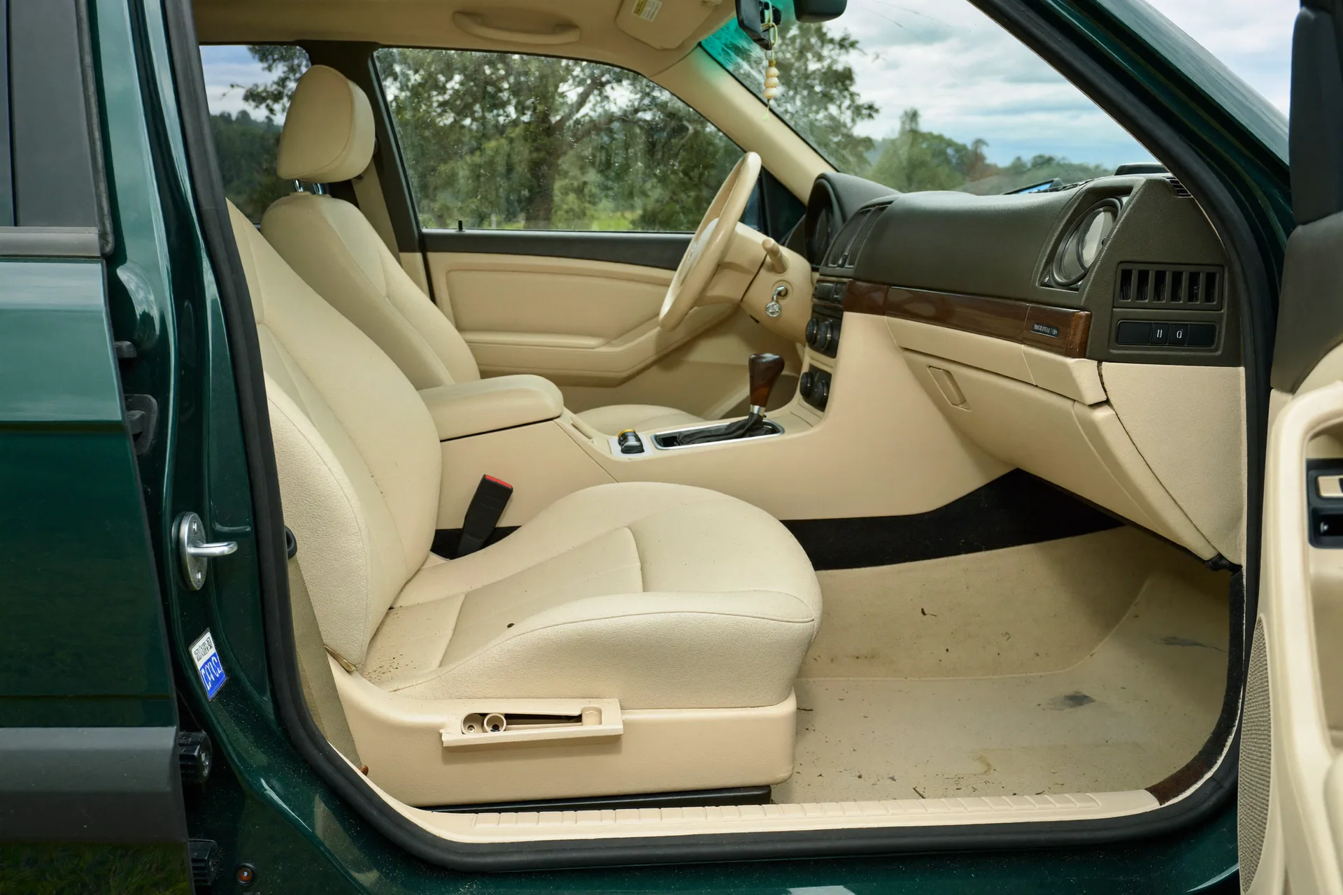 Wide hero composition inside the cream cabin of a forest green hatchback during interior detailing
